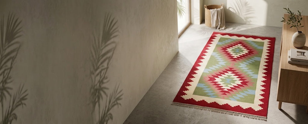 Red, green and cream kilim rug with diamond medallions on a sunlit concrete floor