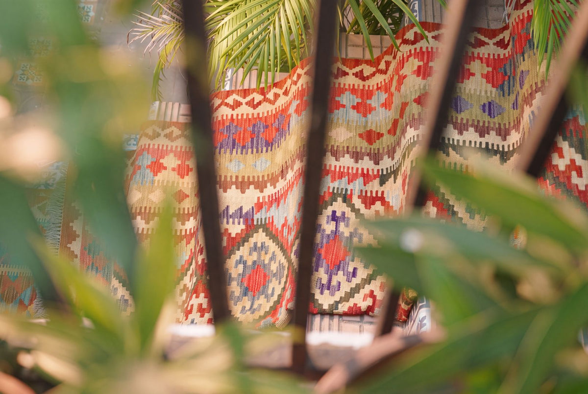 A Maimana kilim draped over a garden wall, seen through palm leaves
