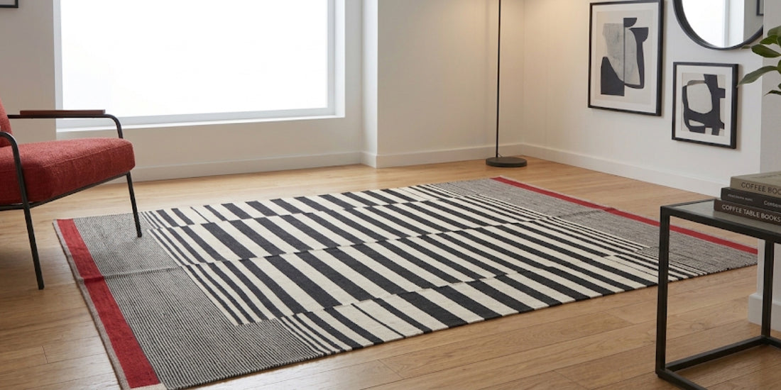 Black and white striped rug with a red edge on an oak floor, beside a red armchair in a bright room