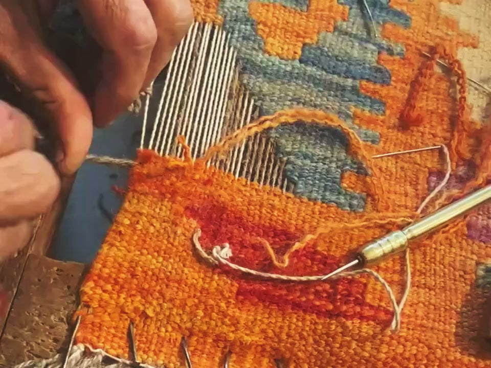 Hands passing wool through the warp threads of a kilim
