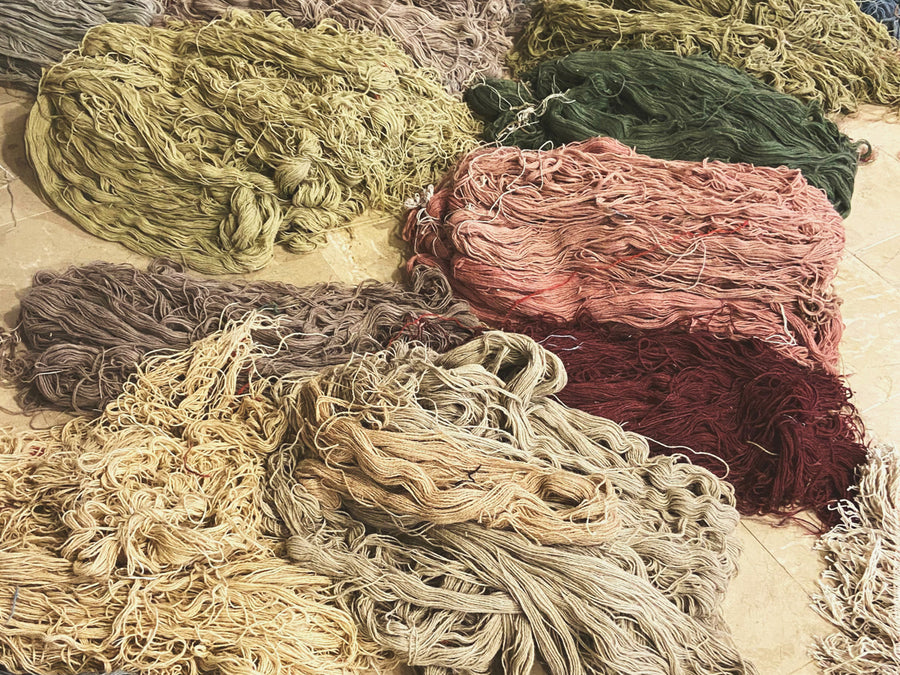 Hanks of hand-spun wool yarn in plant-dyed colours laid out on the floor